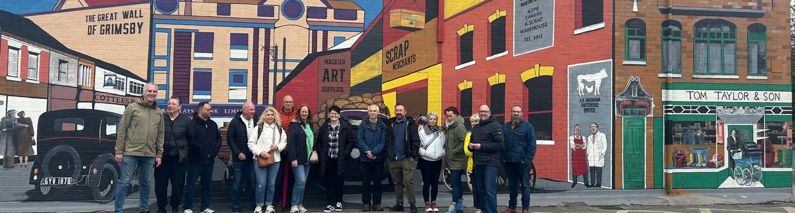 Members of the Growing Together community standing in front of the Great Wall of Grimsby mural